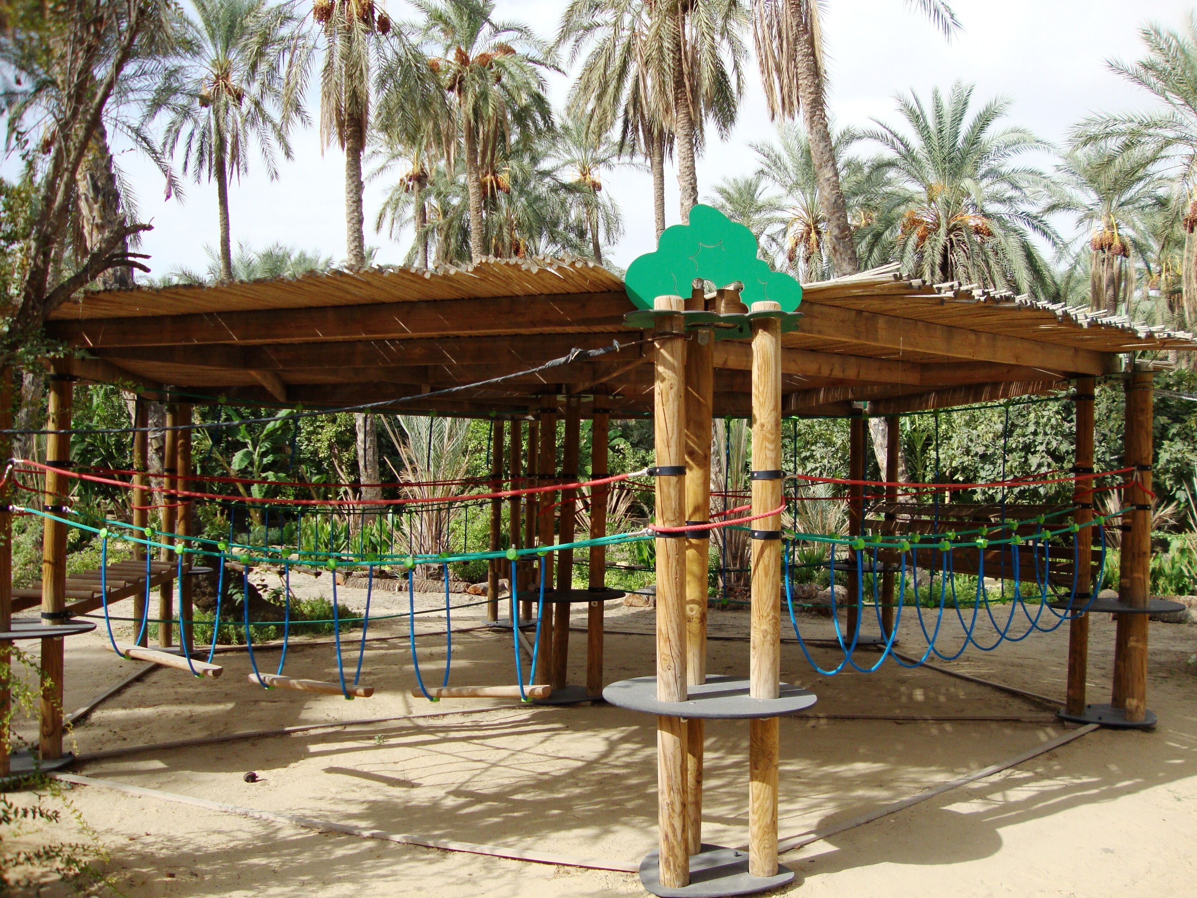 Una estructura de madera con un laberinto de cuerdas, rodeada de palmeras.