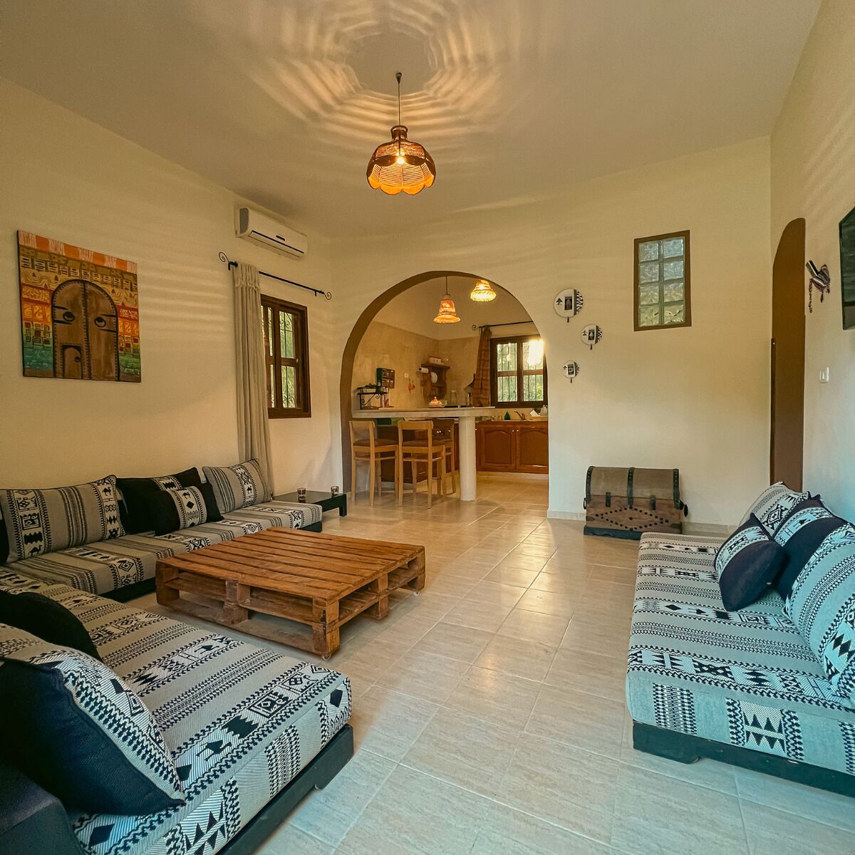 A spacious living room with a sofa set, a wooden coffee table, and a kitchen visible through an archway.