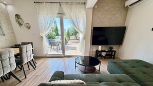 En stue med en grøn sofa, et sofabord, et fjernsyn og et spiseområde med stole og et bord.