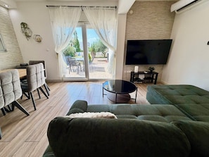 A living room with a green sofa, a coffee table, a TV, and a dining area with chairs and a table. - Spacious 3-bedroom apartment in gorgeous Podstrana (Podstrana - Sv. Martin)