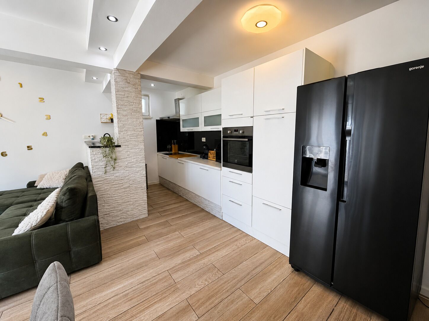 A modern kitchen with white cabinets, a black refrigerator, and a stone pillar.