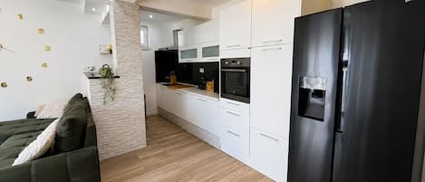 A modern kitchen with white cabinets, a black refrigerator, and a stone pillar.