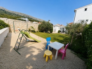 A children's play area with a slide, a table, and chairs, surrounded by a stone wall and greenery. - Spacious 3-bedroom apartment in gorgeous Podstrana (Podstrana - Sv. Martin)