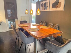 A dining area with a wooden table, grey upholstered chairs, woven placemats, pendant lighting, and abstract wall art. - Modern Luxury Villa Antonia (Mössingen)