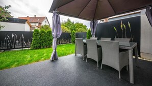 Eine Terrasse im Freien mit Korbmöbeln und einem großen Sonnenschirm.