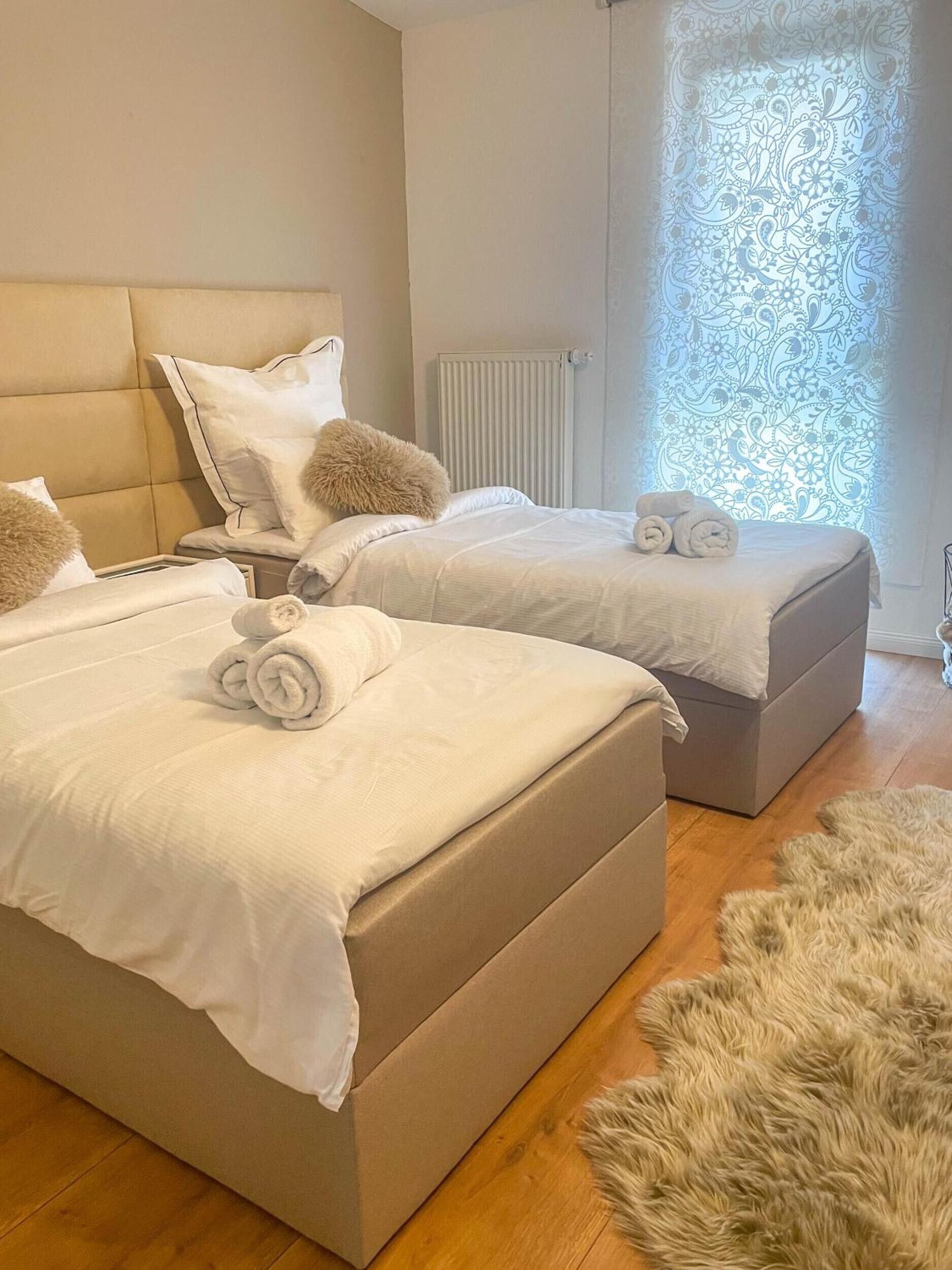 A hotel room with two beds, a fluffy rug, and a window with a patterned curtain.
