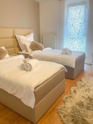 A hotel room with two beds, a fluffy rug, and a window with a patterned curtain.