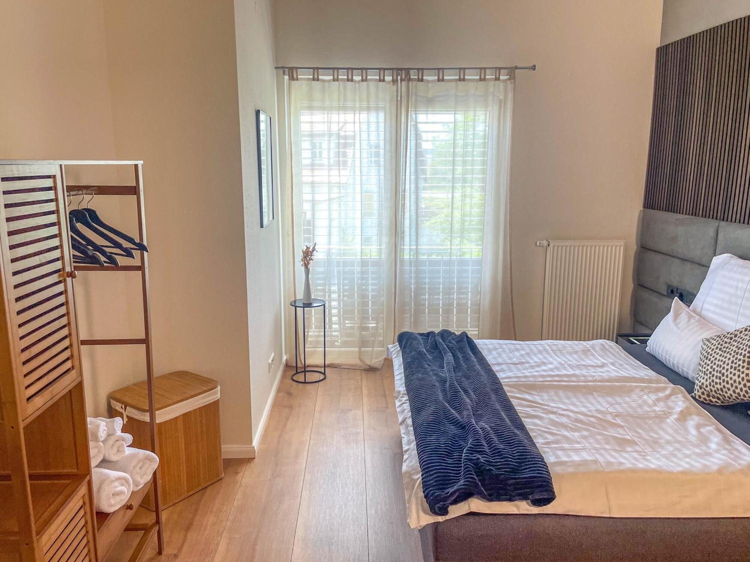 Ein Schlafzimmer mit Bett, Kleiderschrank, Heizkörper und einem Fenster mit Jalousien.