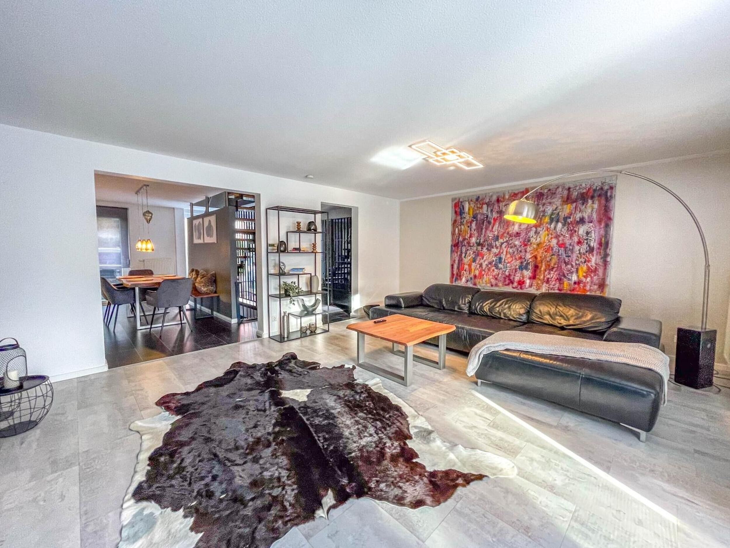 A modern living room with a leather sofa, a coffee table, and a large rug. There is a dining area visible in the background.