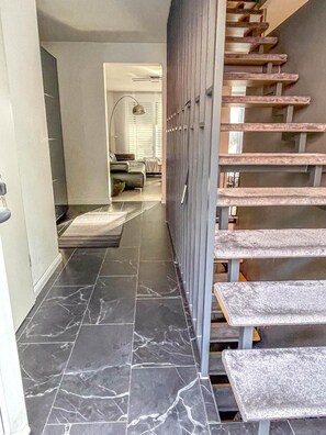 A modern interior with a marble-tiled floor, a staircase with wooden steps, and a view into a living area with a sofa and a lamp. - Modern Luxury Villa Antonia (Mössingen)