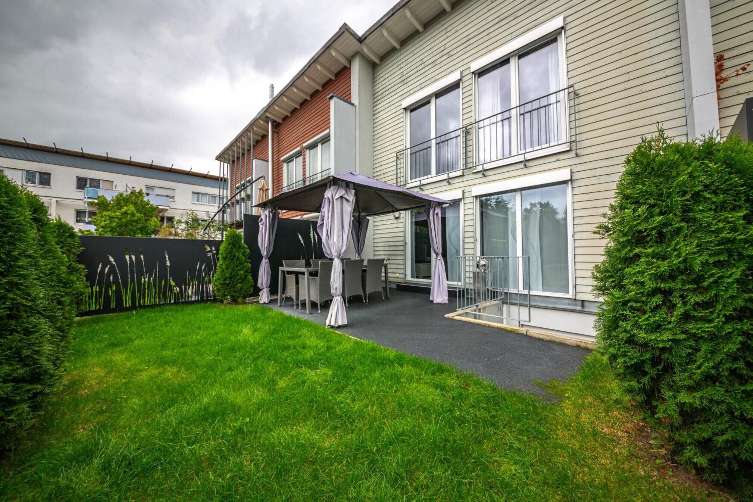 A residential building with a covered patio area, a small lawn, and a metal fence.