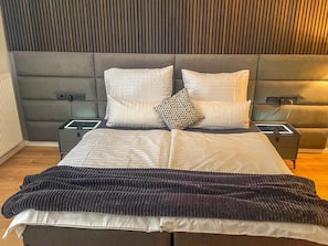 A modern bedroom with a large bed, two bedside tables, and a headboard with vertical lines.