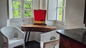 Ein Eckzimmer mit zwei Korbstühlen, einem Holztisch und einem roten Sessel.