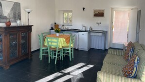 Ein Zimmer mit Esstisch, Stühlen, einer Couch, einer Küchenzeile inklusive Herd und Spüle sowie einem Fenster.