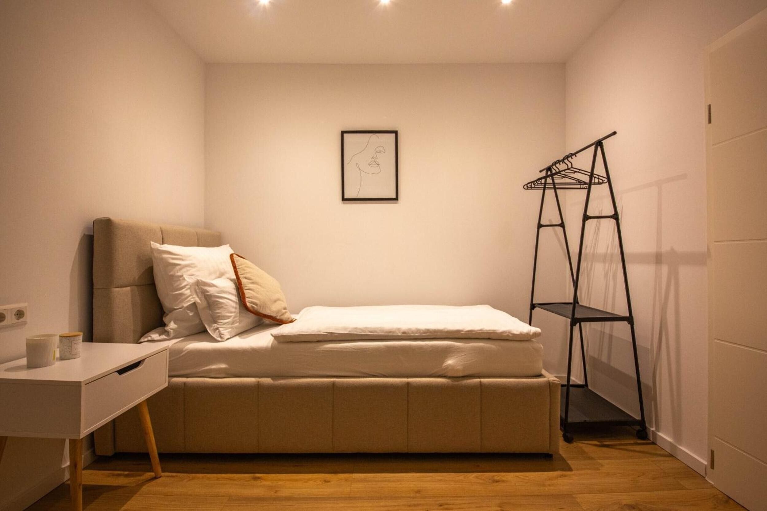 A small, neatly arranged bedroom with a bed, a desk, and a wall-mounted shelf.