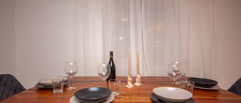 Une table à manger dressée avec des assiettes, des verres et des bougies, une bouteille et un chandelier posés sur la table.