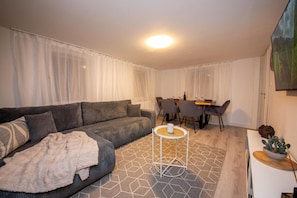 A modern living room with a grey sofa, a coffee table, and a dining area with chairs and a table.