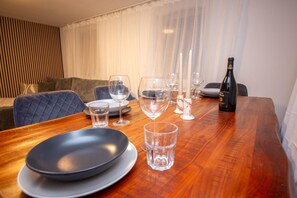 A dining table set with plates, glasses, and a bottle, with a sofa and curtains in the background.