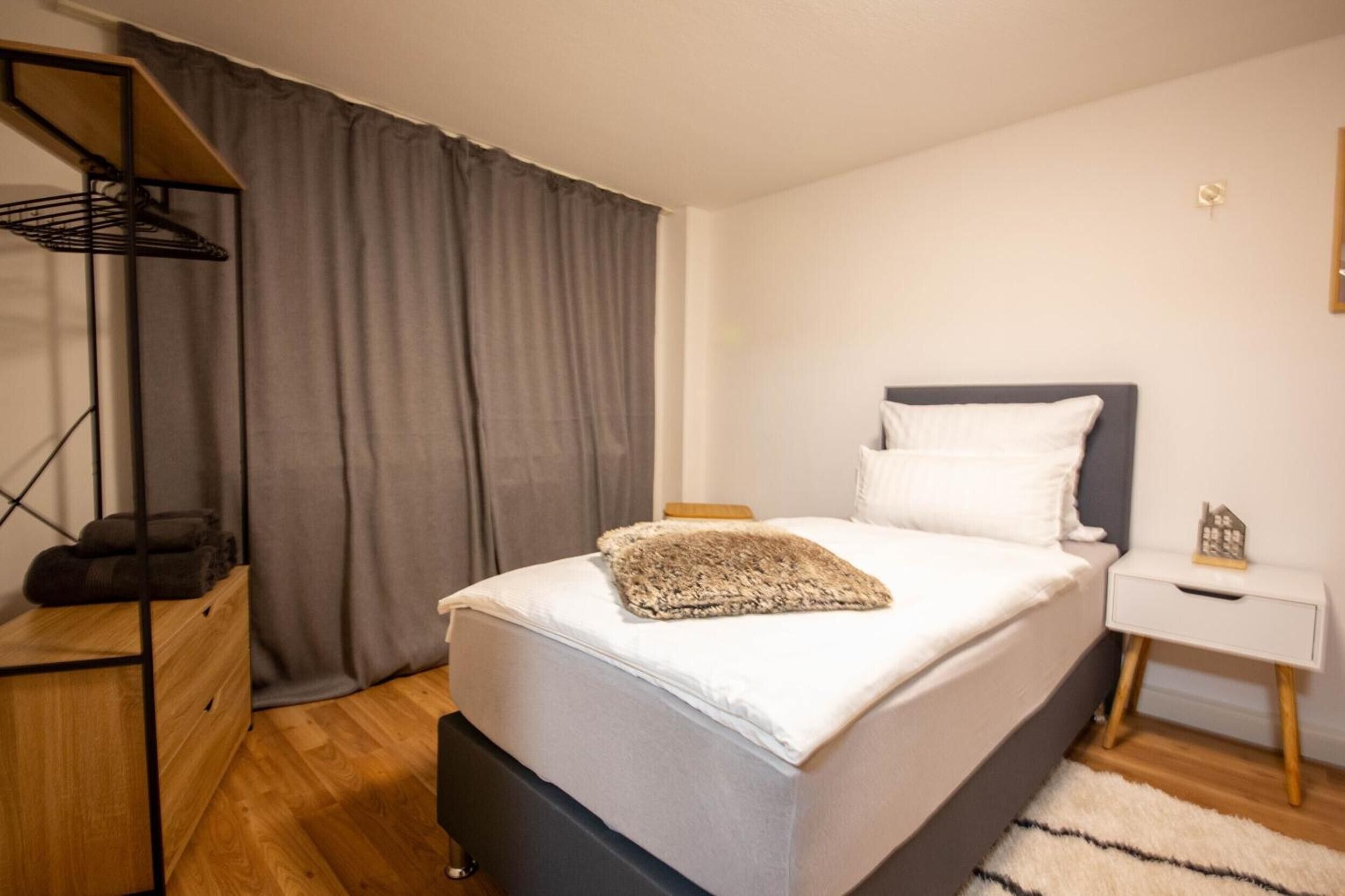 A bedroom with a bed, a nightstand, a lamp, and a wardrobe.
