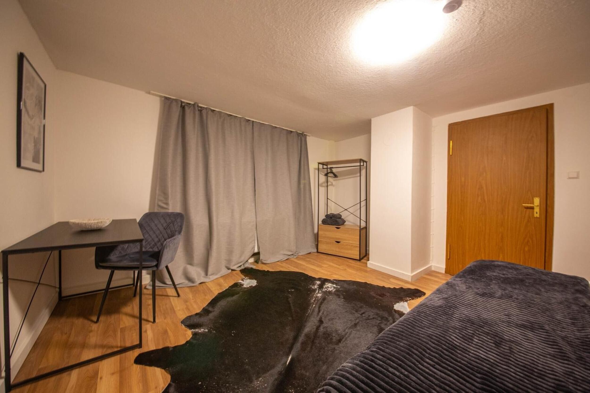 Ein Zimmer mit Schreibtisch, Stuhl, Bett und Spiegel.
