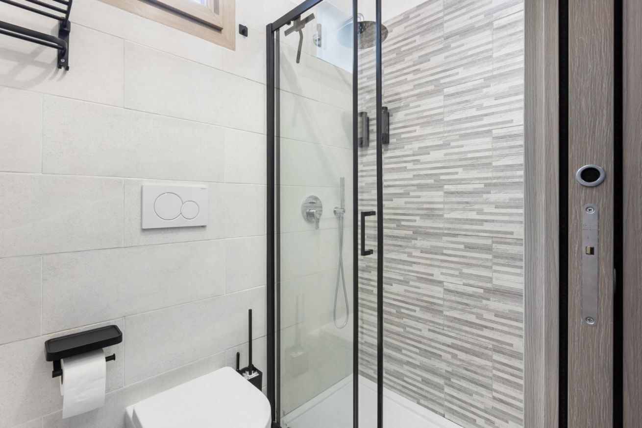 A modern bathroom with a glass shower enclosure, a toilet, and a towel dispenser.