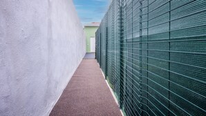 A narrow corridor with a textured floor, a green metal fence on one side, and a white wall on the other. - An elegant suite within a multi-unit property, ideal for two guests, featuring ground-floor access (with a single step at the entrance).The property is located in the center of Selargius—a town situated approximately 6.5 km from Cagliari’s city cente (Selargius)