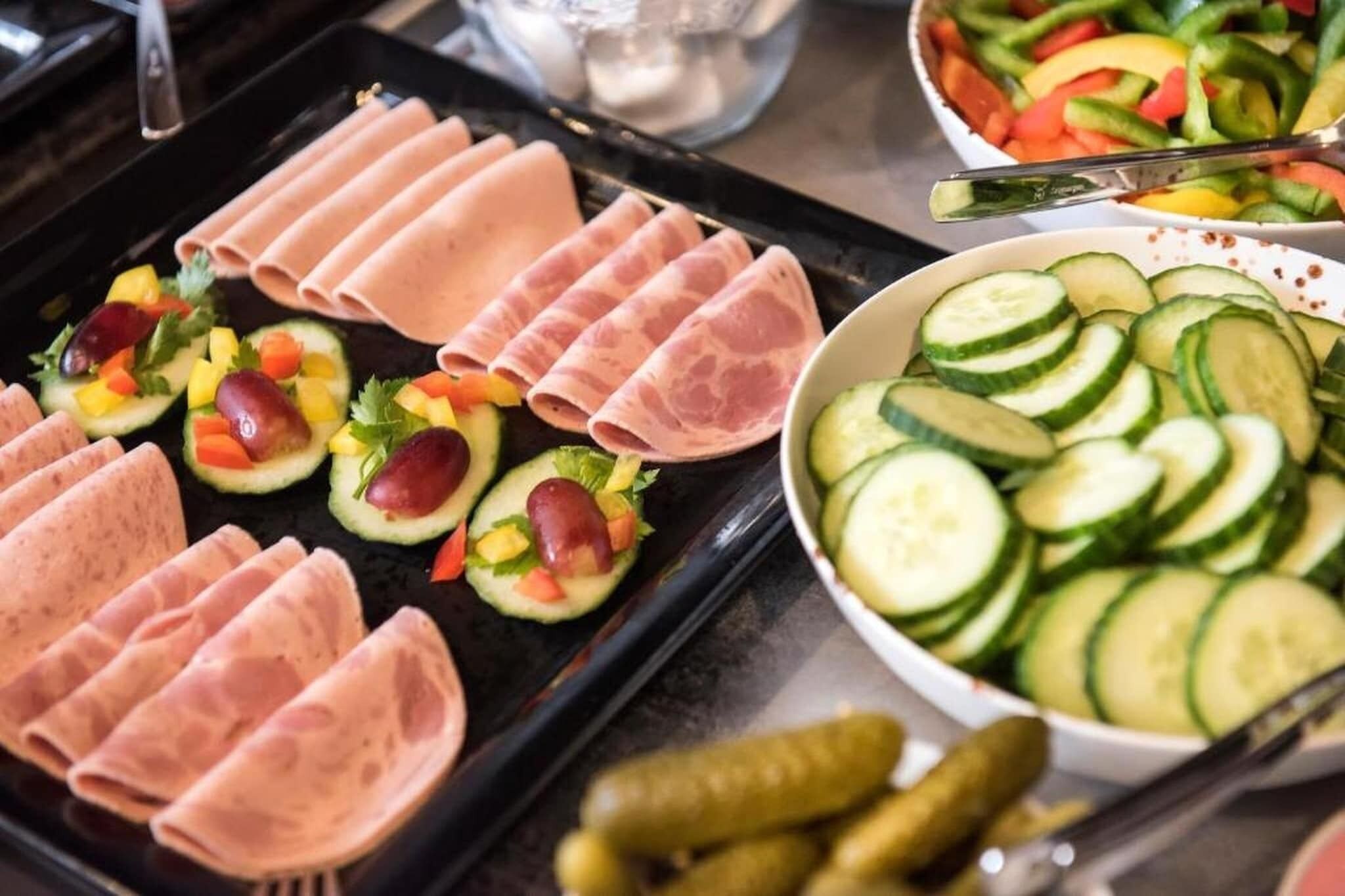 Une table de buffet avec des viandes en tranches, des légumes et des cornichons.