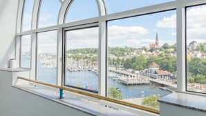 Blick aus einem Fenster mit Geländer auf einen Yachthafen mit Booten und einem Kirchturm in der Ferne.
