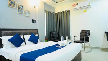 Hotellihuone, jossa on sänky, kaksi tuolia, kirjoituspöytä puhelimineen ja ilmastointilaite.