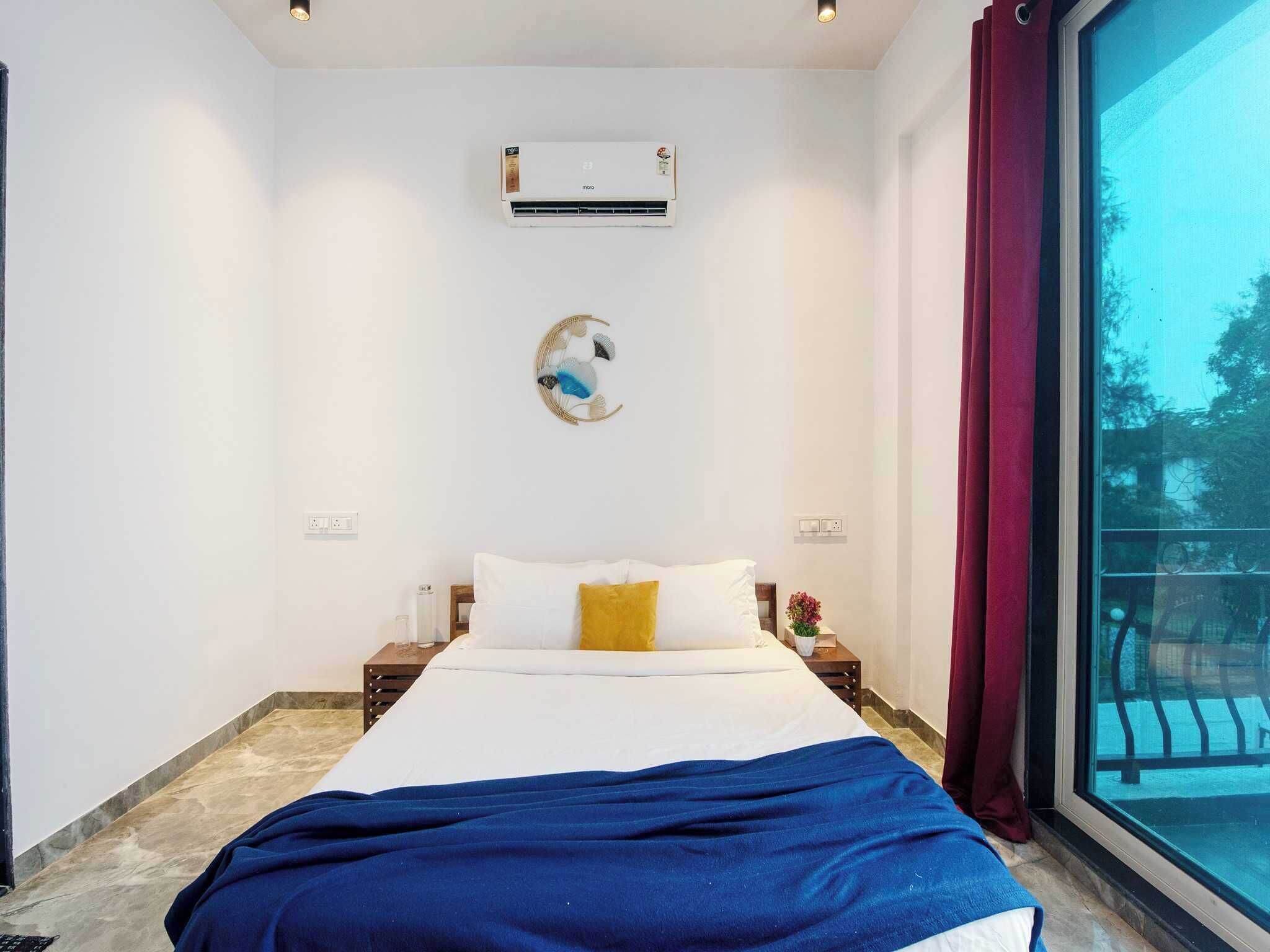 Ein Schlafzimmer mit einem Bett, einer Wandklimaanlage, einem Wandbild und einem Fenster mit Blick ins Freie.