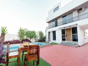 A modern two-story house with a swimming pool, outdoor seating, and a balcony.