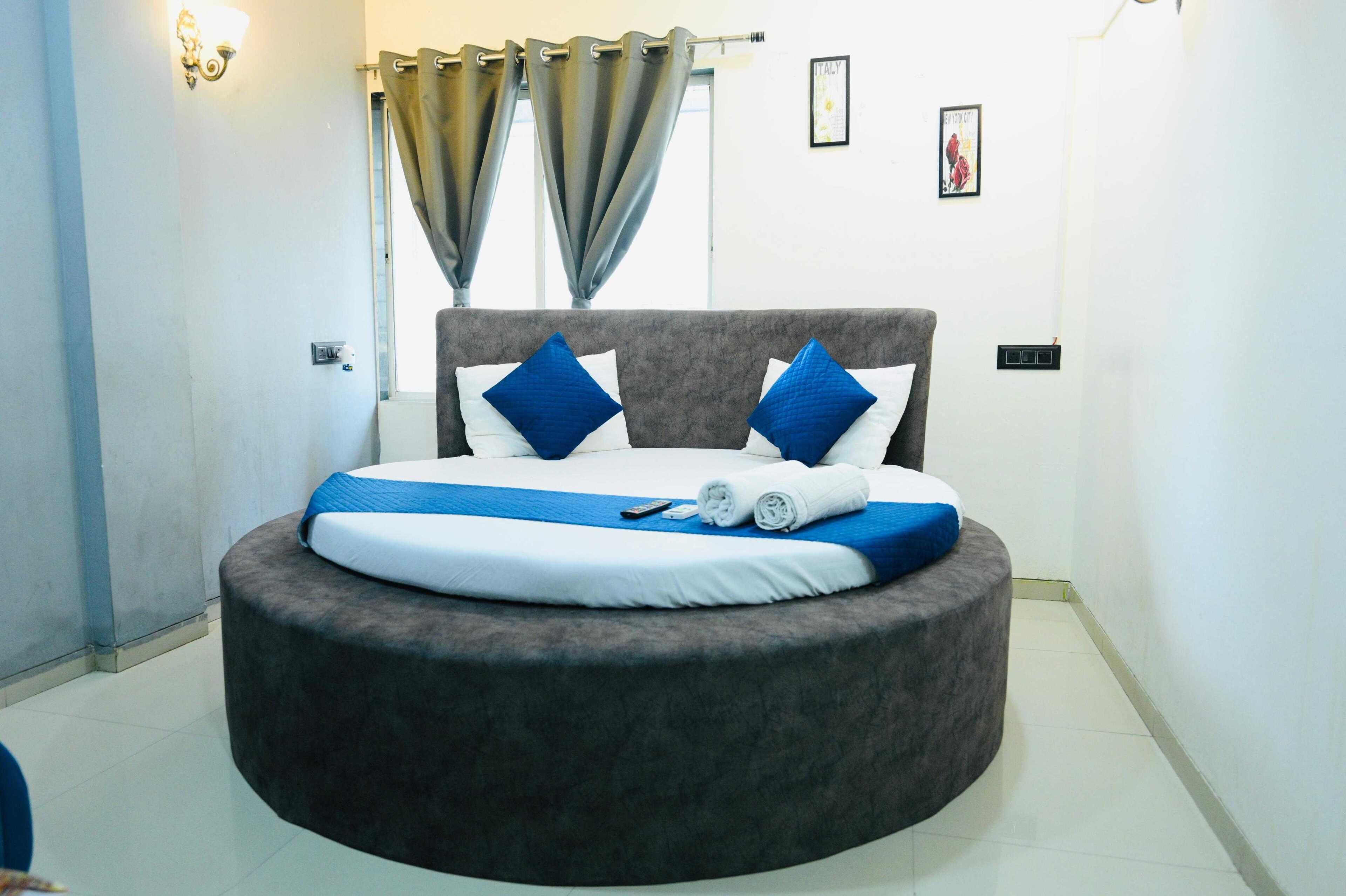 Een rond bed met een grijs hoofdeinde, witte en blauwe kussens en een blauwe deken.