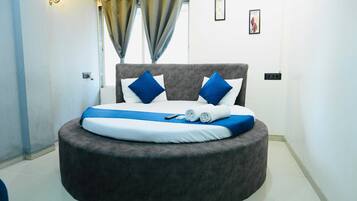 Een rond bed met een grijs hoofdeinde, witte en blauwe kussens en een blauwe deken.