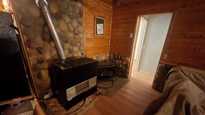 Ein gemütliches Zimmer mit Kaminofen, Steinwand, Holzboden und einer Tür, die nach draußen führt.