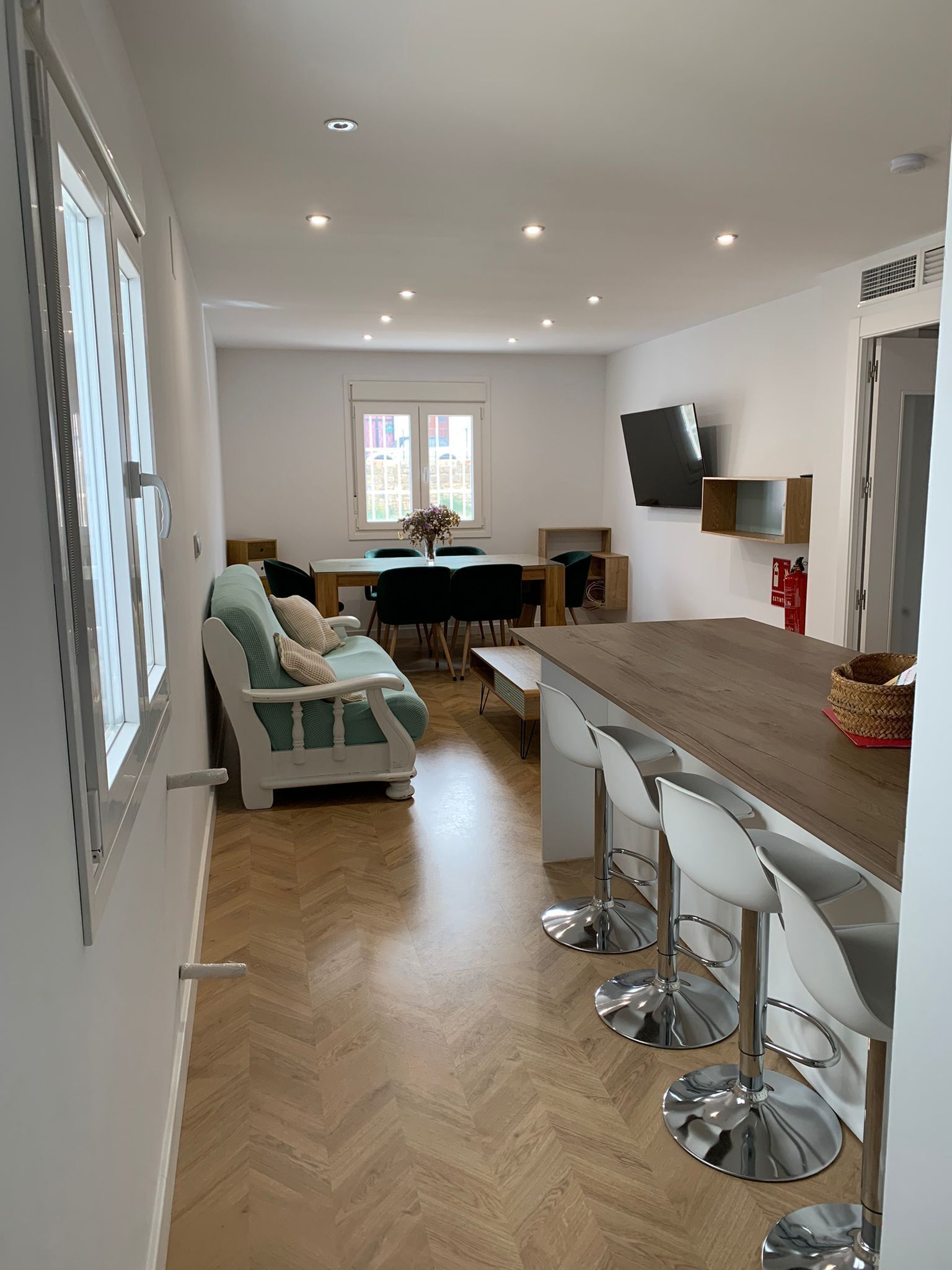 A modern kitchen with a dining area, a sofa, and a TV mounted on the wall.