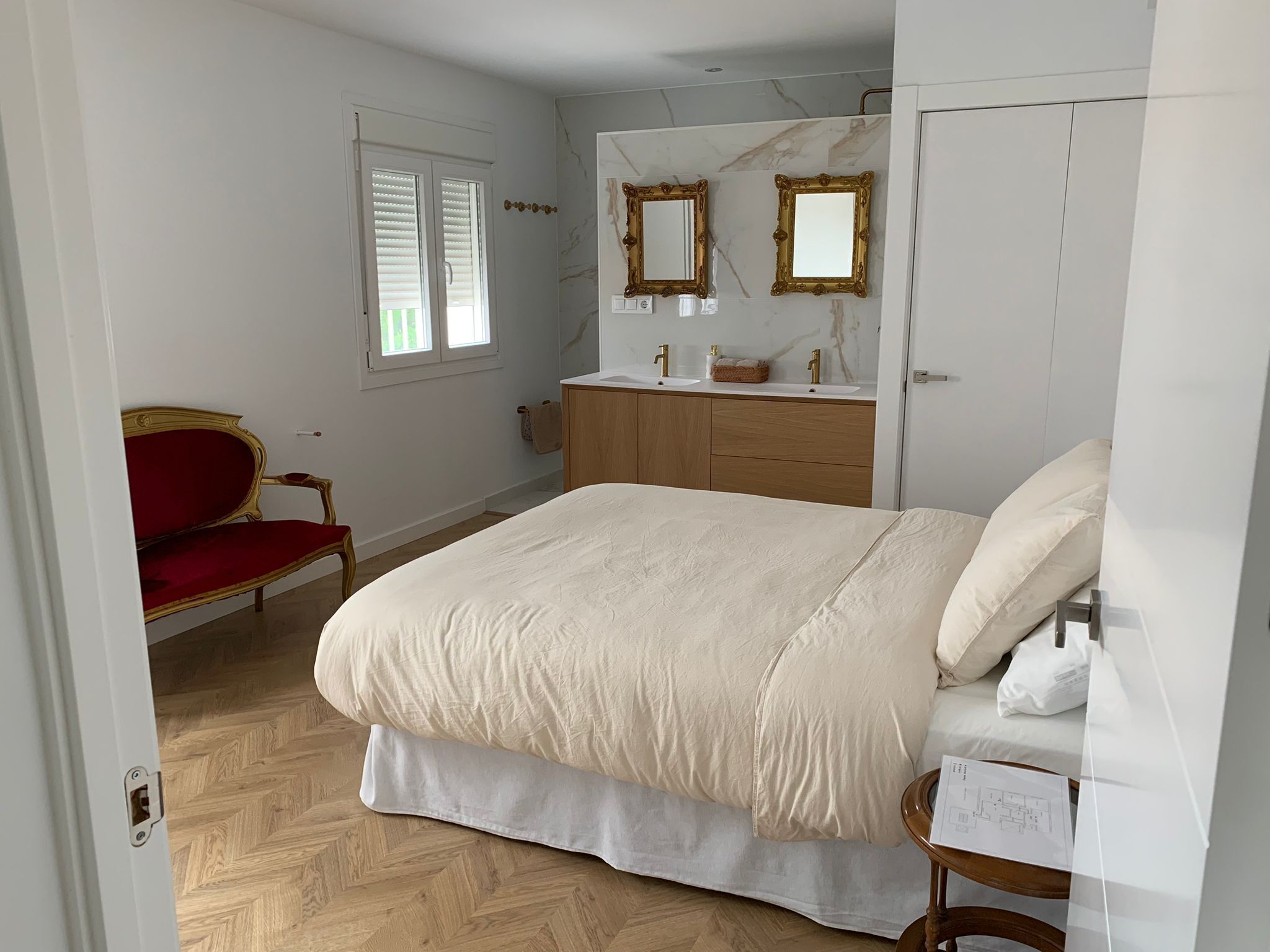 A bedroom with a bed, a vanity with a mirror, a red chair, and a wooden wardrobe.