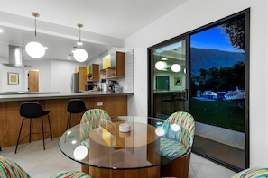 A modern kitchen with a glass dining table, colorful chairs, and a view of a garden through a sliding door. - Solstice Sonora - A Ryson Property (Palm Springs)