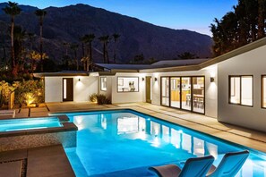Ein Pool mit Bergblick, eine Terrassenfläche und ein Gebäude mit großen Fenstern.
