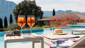 A poolside setting with two glasses of a beverage, a hat, and a cushion on a lounge chair. - MC Como - My Home in Como (Tremezzo)