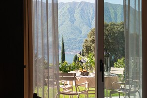 A room with a sliding glass door leading to an outdoor seating area with a table and chairs, overlooking a mountainous landscape. - MC Como - My Home in Como (Tremezzo)