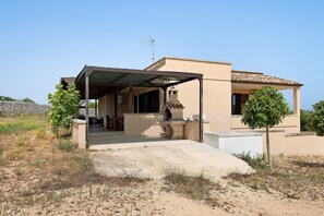 Ein eingeschossiges Haus mit überdachter Terrasse, einer Steinmauer und einem kleinen Baum.