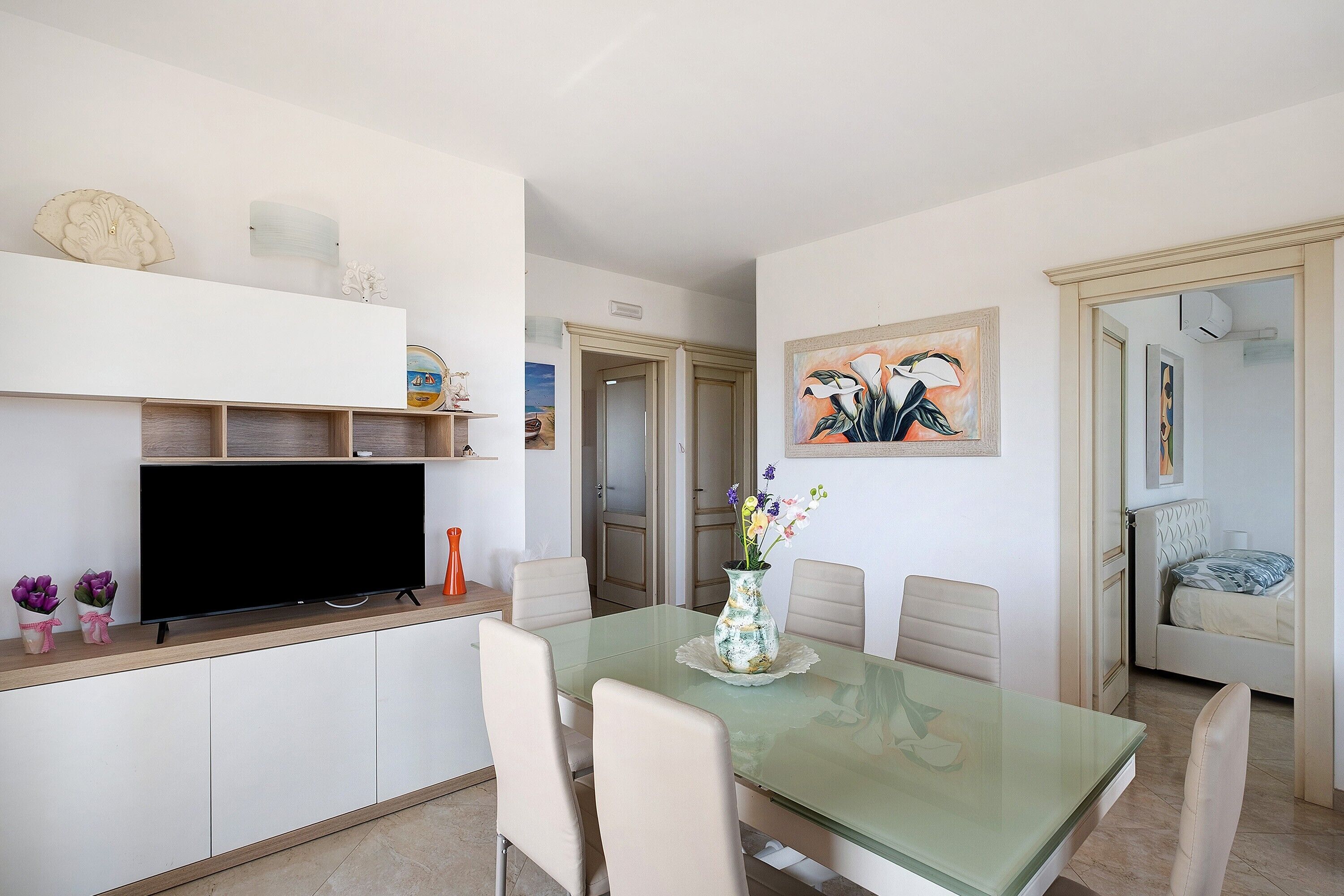 A dining area with a glass table, chairs, a television, and decorative items.