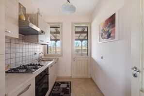 A compact kitchen with a gas stove, oven, and tiled backsplash. There is a wooden door leading to a balcony with a view of trees. - Villa 'Adg House' with Shared Terrace, Wi-Fi and Air Conditioning (Otranto)