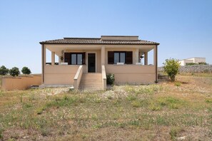 Ein eingeschossiges Haus mit einem Ziegeldach, einer Veranda und einem Hauseingang.