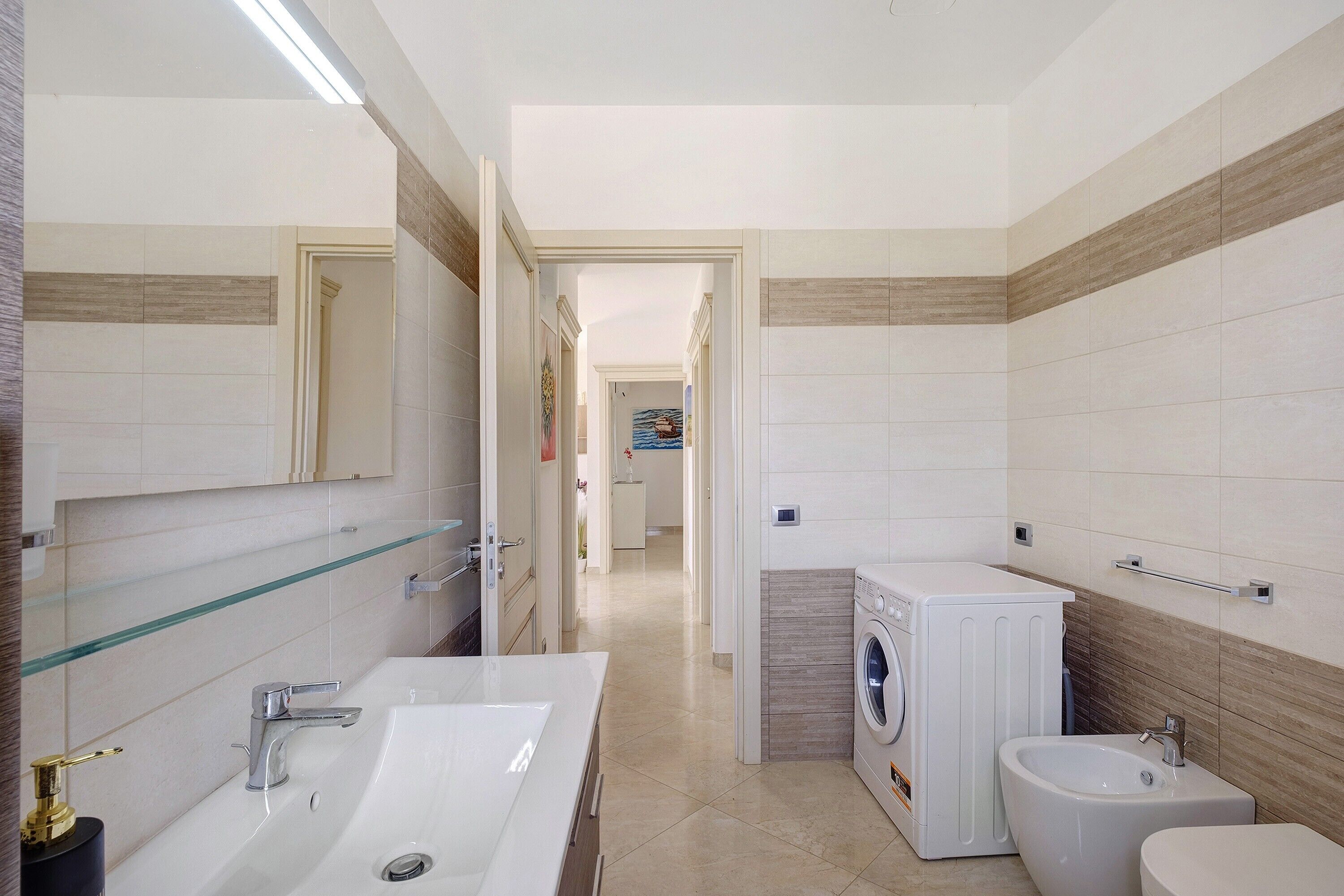 Ein modernes Badezimmer mit einem großen Spiegel, einem weißen Waschbecken, einer Waschmaschine und einem Bidet.