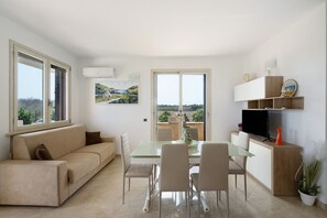 Ein stilvolles Wohnzimmer mit einer Couch, einem Esstisch, Stühlen, einem Fernseher und Kunstwerken.