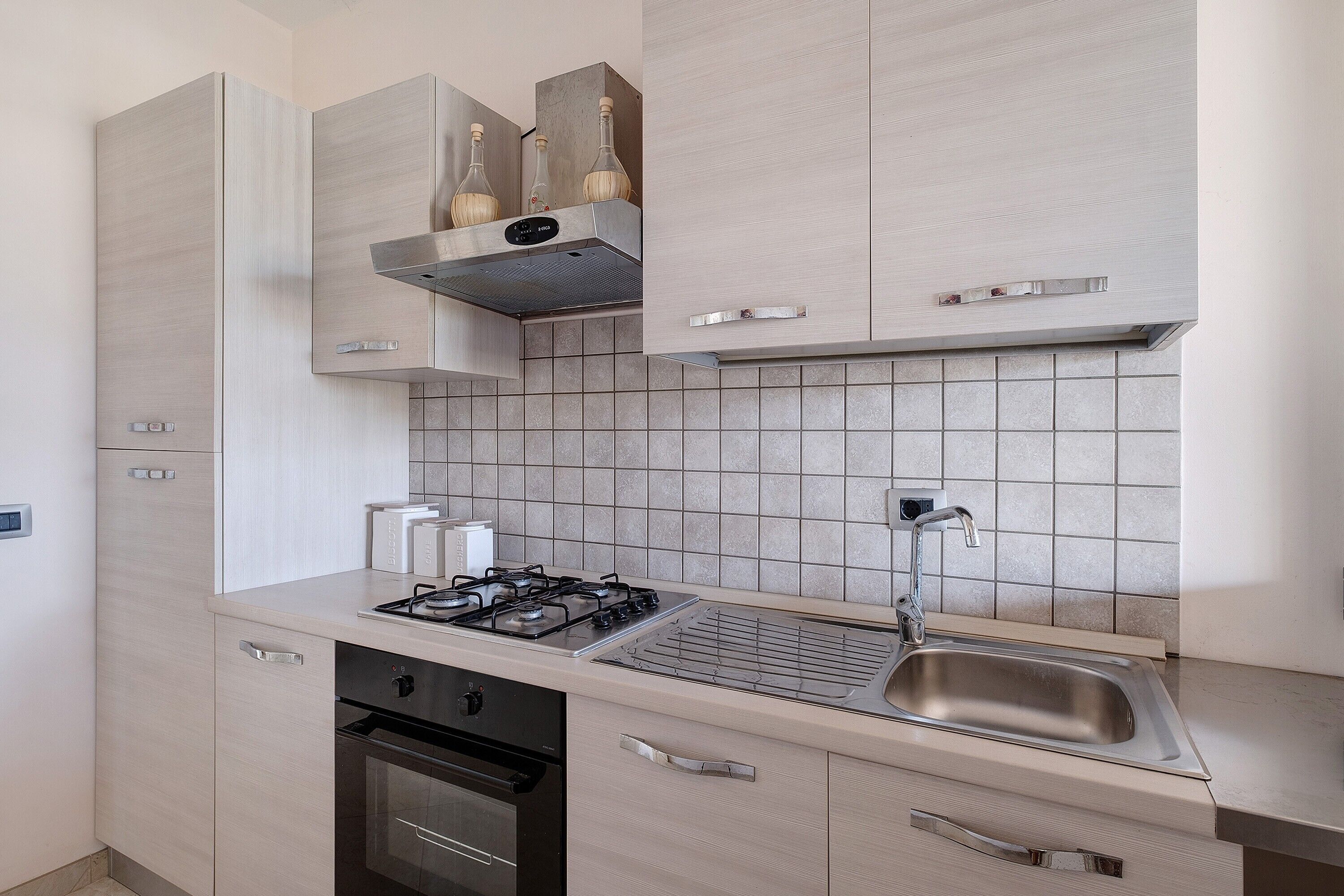 Une cuisine moderne équipée d’une cuisinière à gaz, d’un four encastré, d’un évier en acier inoxydable et de meubles de rangement de couleur claire.