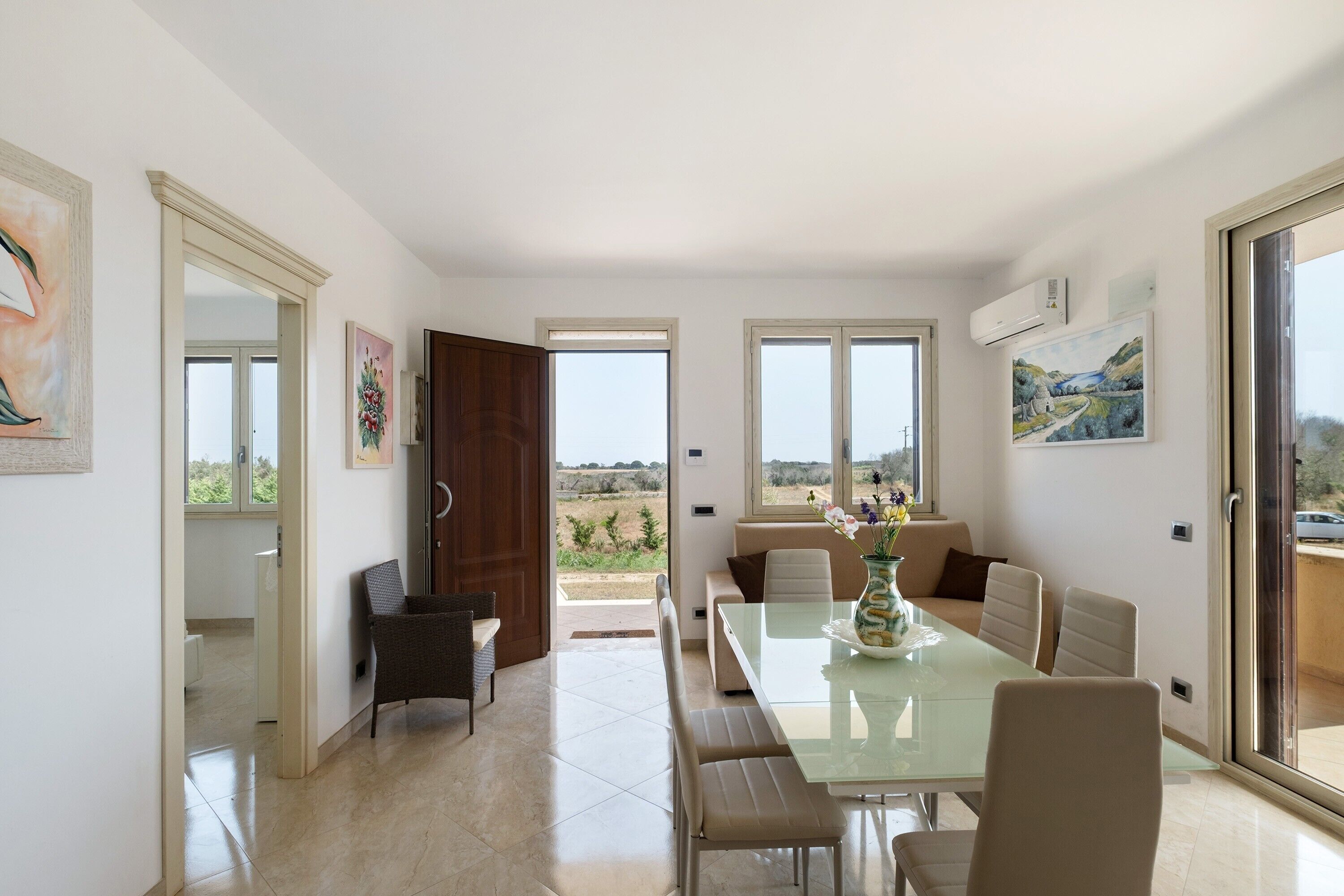 Zona pranzo con tavolo in vetro, sedie e vista sull'esterno.