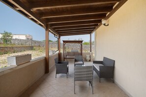 A covered patio area with wicker furniture and a stone wall in the background. - Villa 'Adg House' with Shared Terrace, Wi-Fi and Air Conditioning (Otranto)