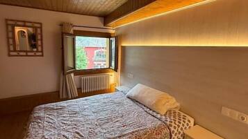 A bedroom with a wooden ceiling, a bed with patterned bedding, a bedside table, and a window with a view.